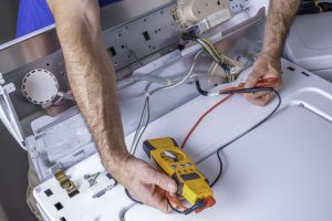 Hands of an appliance technician troubleshooting or repairing a washing machine